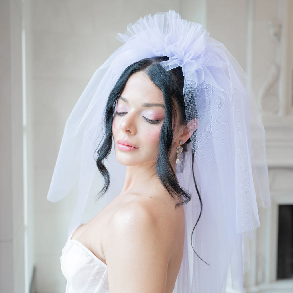 Woman wearing a white wedding dress and lilac colour veil indoors.