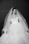 Black and white photo of a bride in a wedding dress with a long veil against a dark background