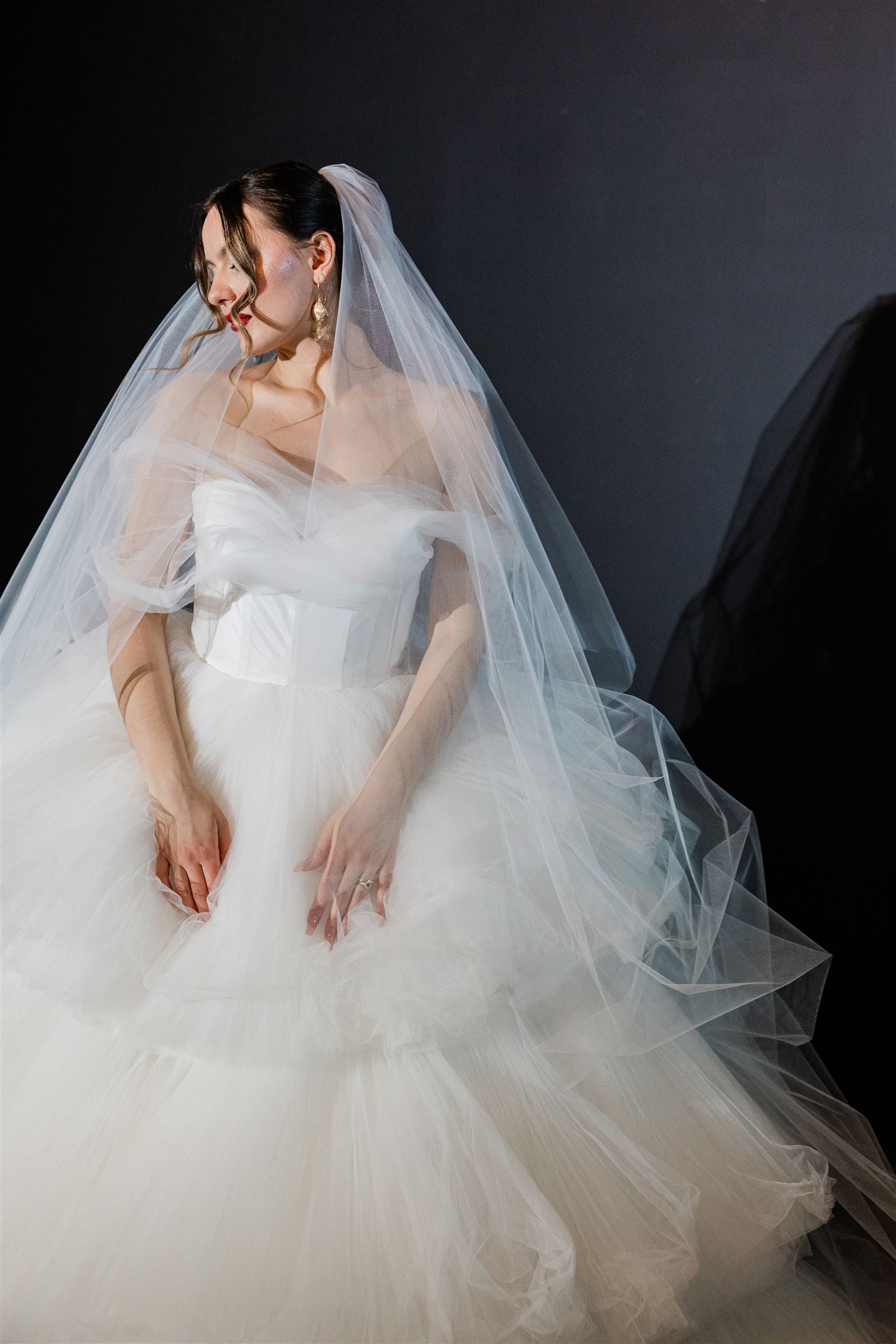 Bride in a white wedding dress with a long veil against a dark background