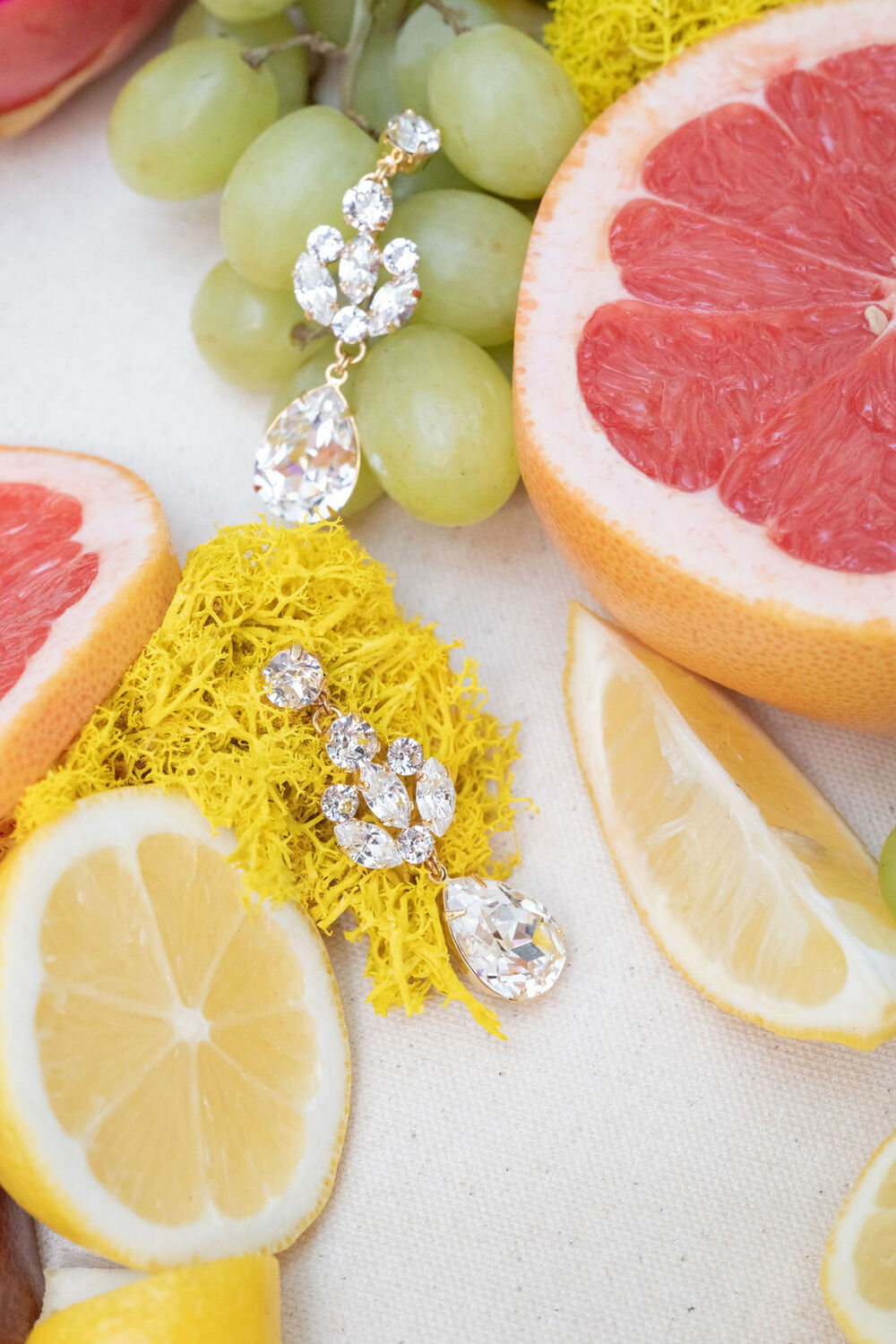 Jewelry with yellow tassels and crystals on a background of sliced fruits including lemons, grapefruit, and grapes.