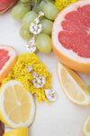 Jewelry with yellow tassels and crystals on a background of sliced fruits including lemons, grapefruit, and grapes.