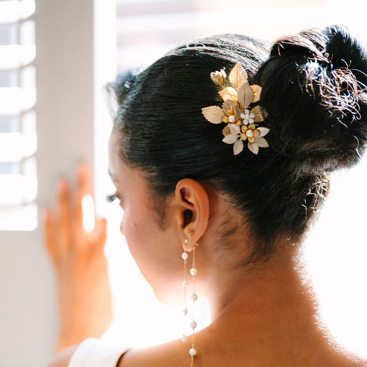 Woman with elegant hairpiece and pearl drop earrings, wearing a white dress, in a softly lit room.