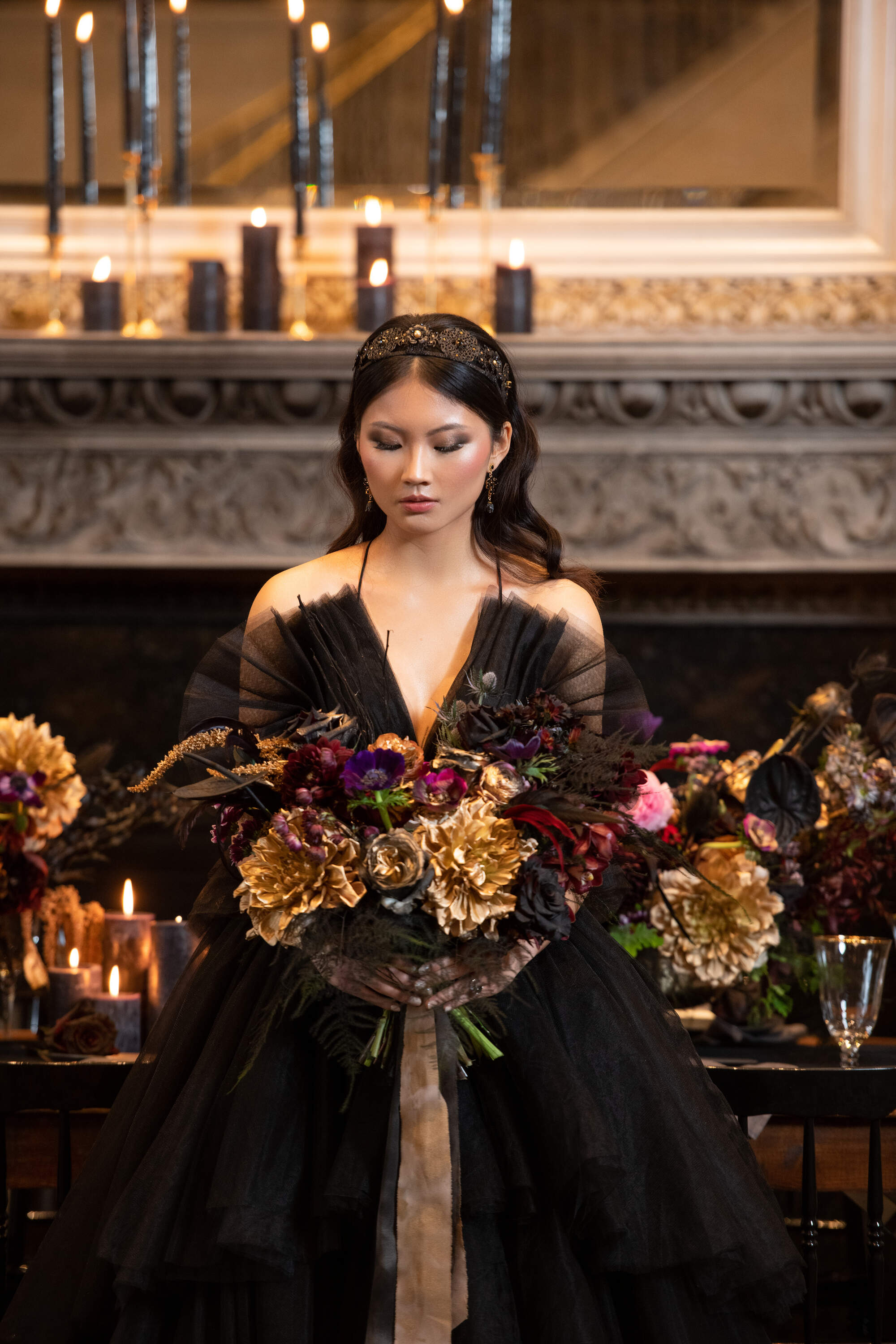 Woman in a black gown holding a bouquet of flowers in a dimly lit room with candles and decorative elements.
