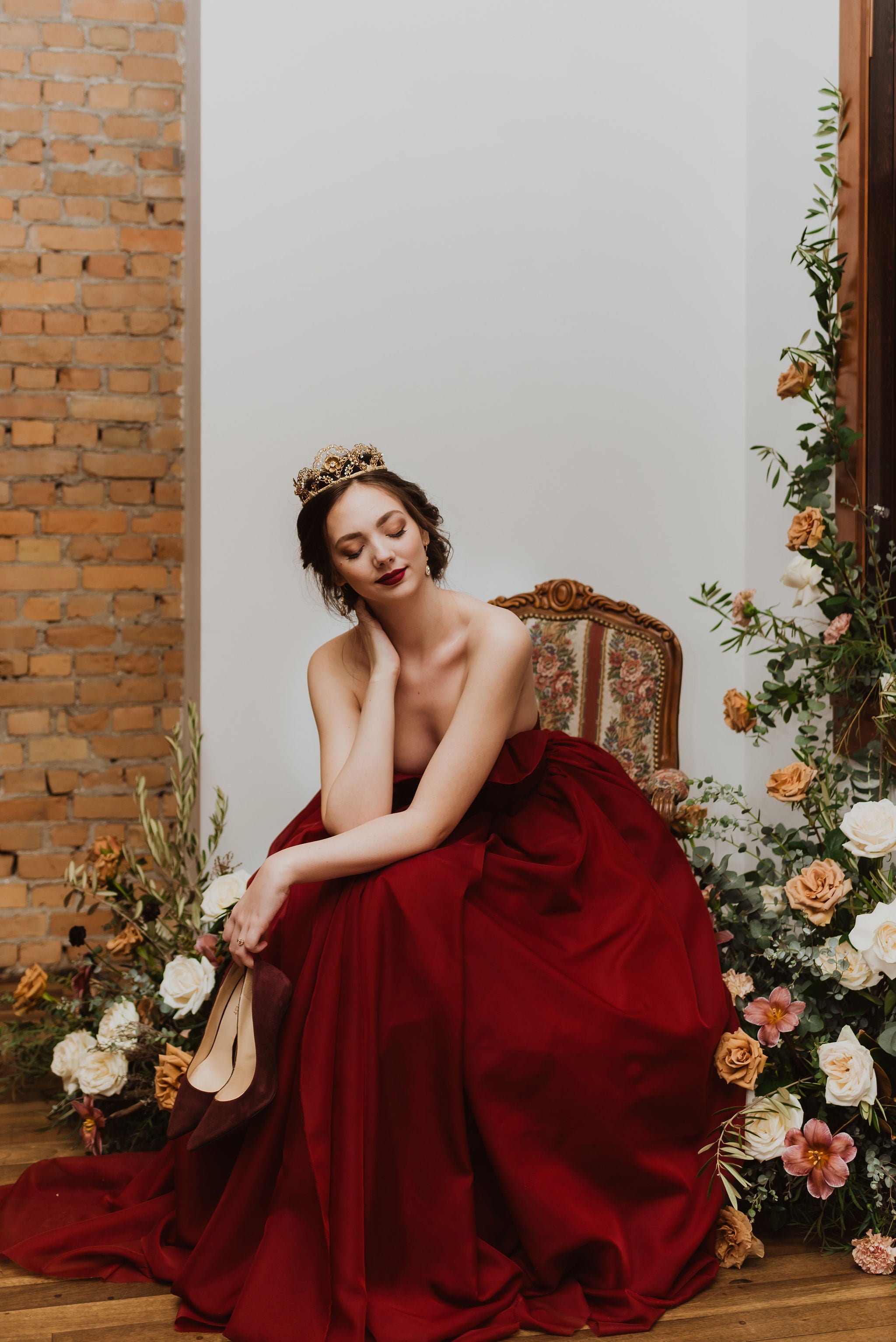 Woman in a red dress sitting on a chair with floral decorations and a brick wall in the background