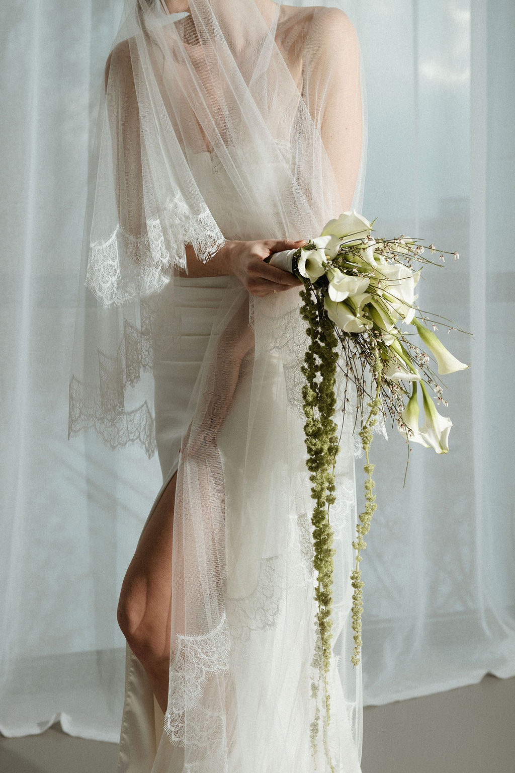 Bride holding a bouquet of flowers with a white veil in the background