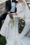 Couple in wedding attire sitting outdoors with a stone wall background