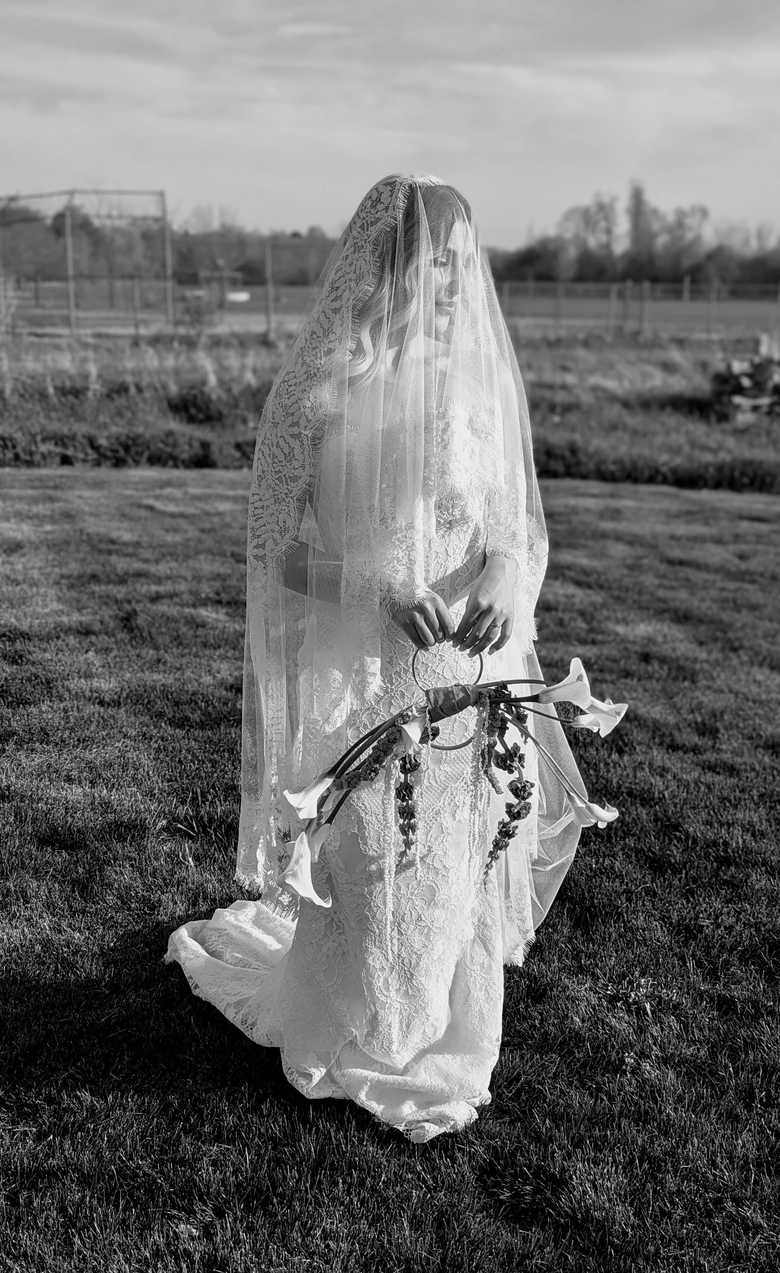 Person in a long, light-colored dress with a veil standing in a grassy field.