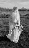 Person in a long, light-colored dress with a veil standing in a grassy field.