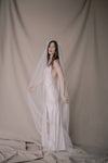 Woman in a white wedding dress with a veil against a plain background