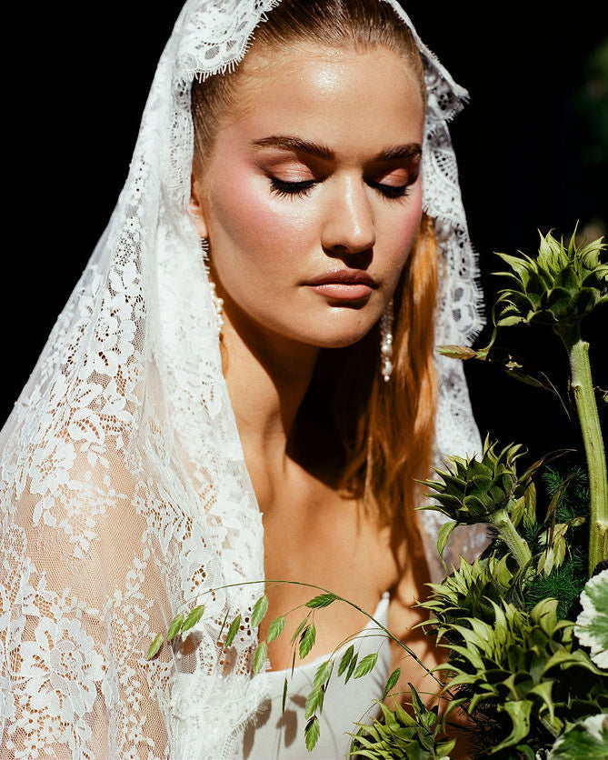 Woman wearing a lace veil holding a bouquet of flowers against a dark background