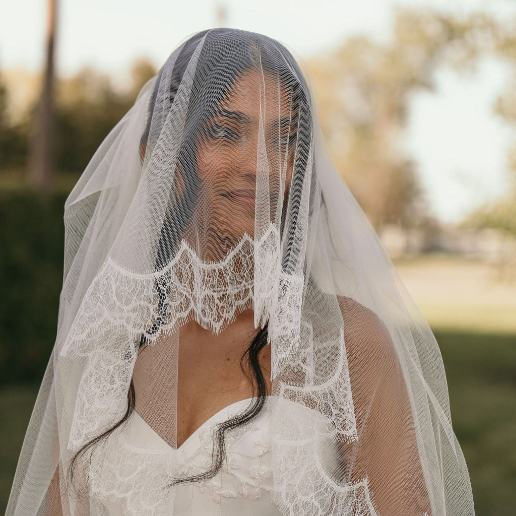 Woman wearing a white wedding dress with a lace veil outdoors.
