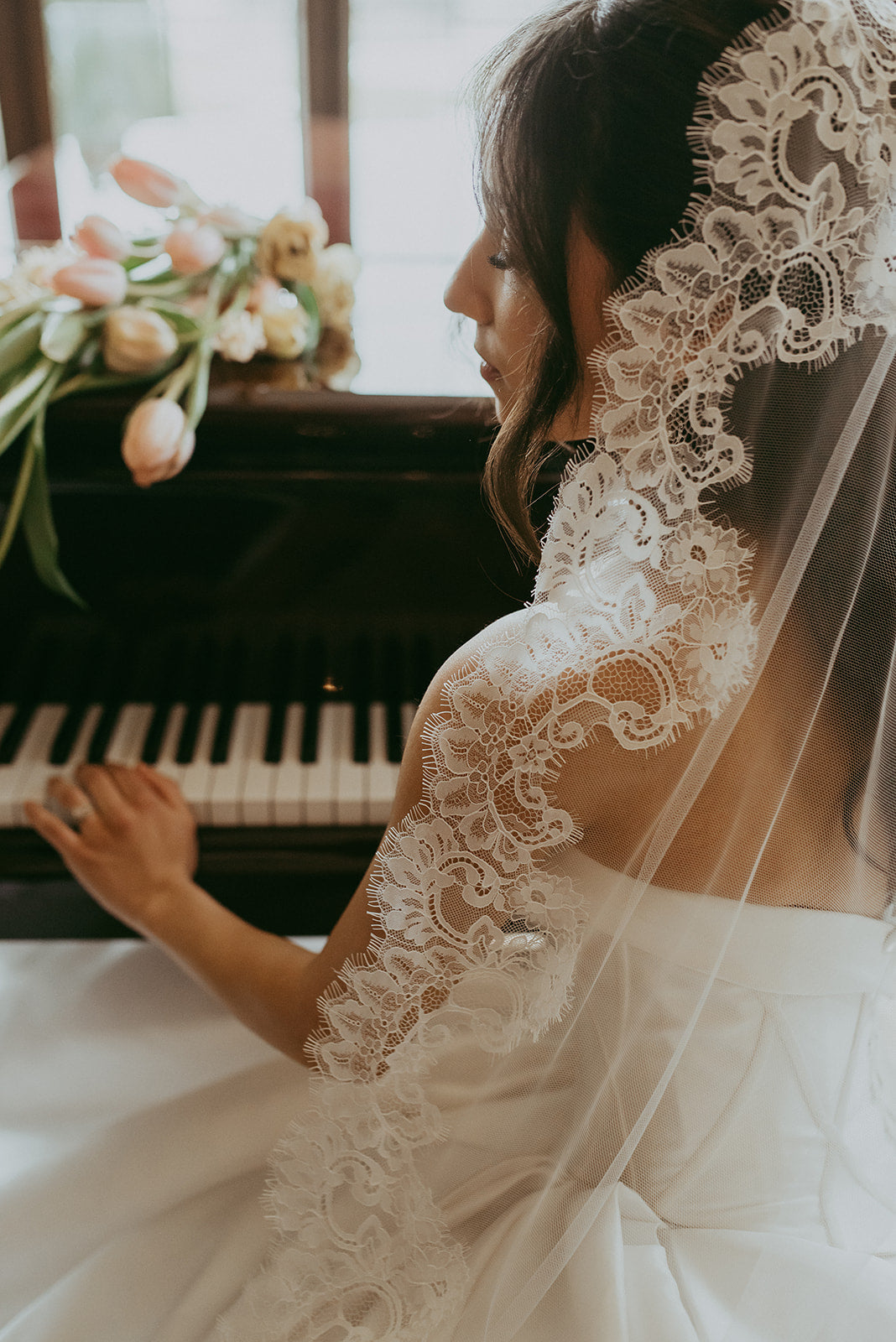 Bride in a white wedding dress with a lace veil sitting at a piano.