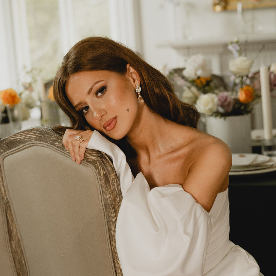Woman in a white dress sitting on a couch in a decorated room with flowers and candles.