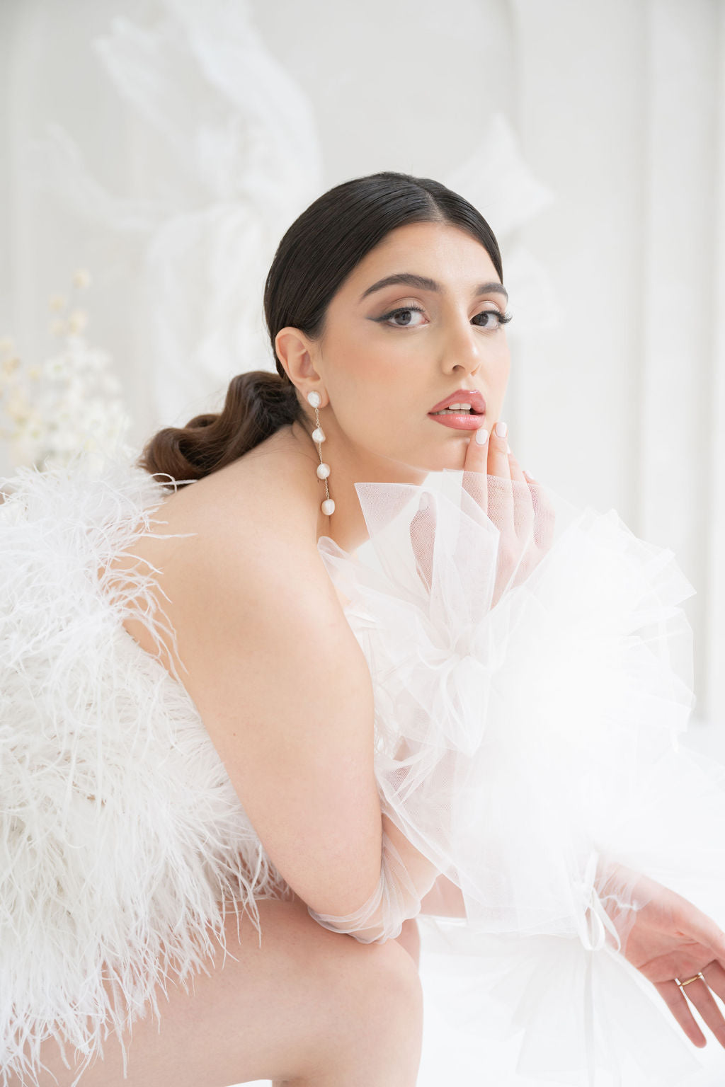 Woman wearing a white feathered outfit with long freshwater pearl bridal earrings against a white background
