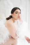 Woman wearing a white feathered outfit with long freshwater pearl bridal earrings against a white background