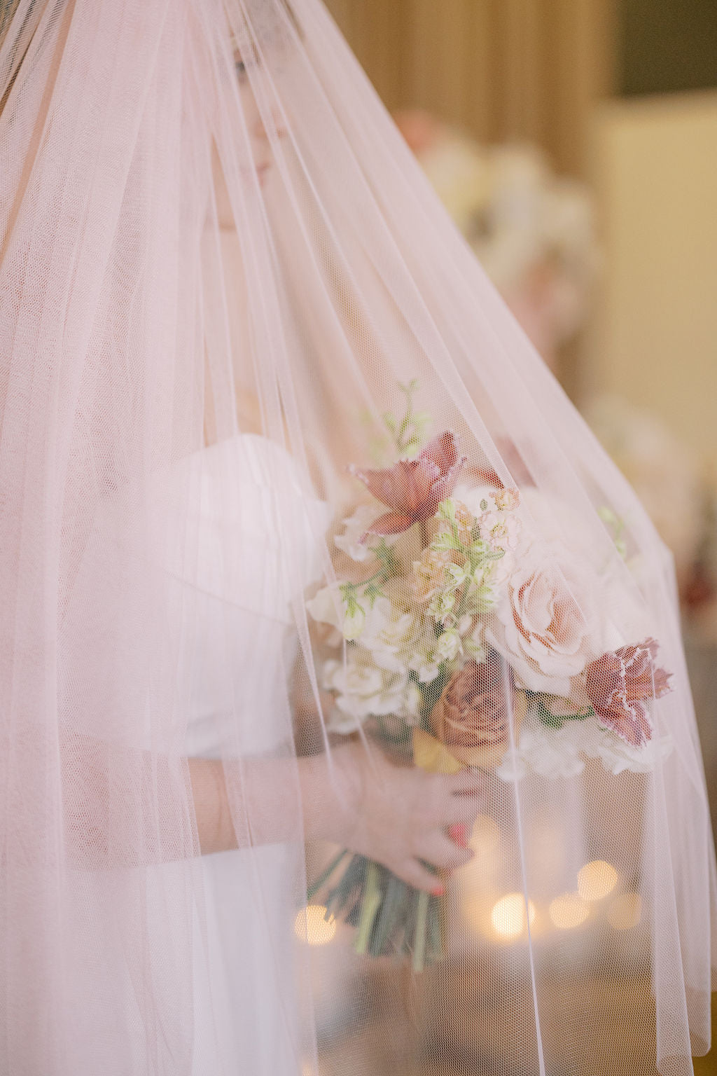 Bride holding a bouquet under a veil with blurred lights in the background