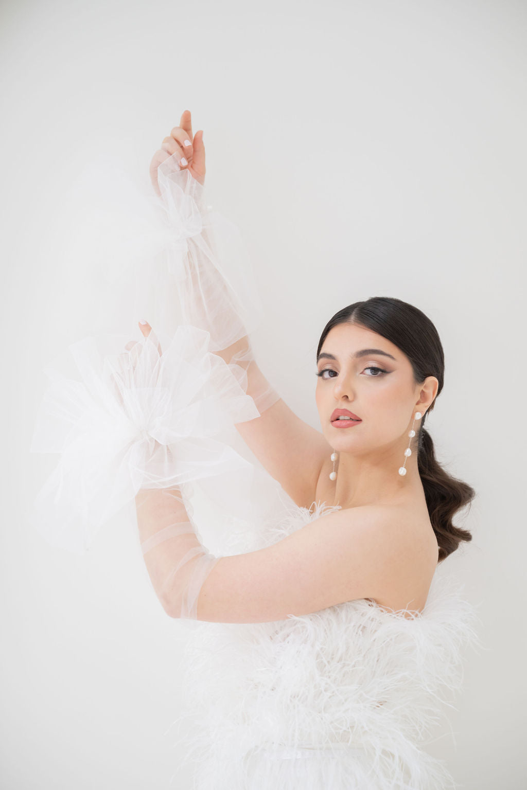 Woman in a white wedding dress with long gloves with baroque pearl earrings against a white background