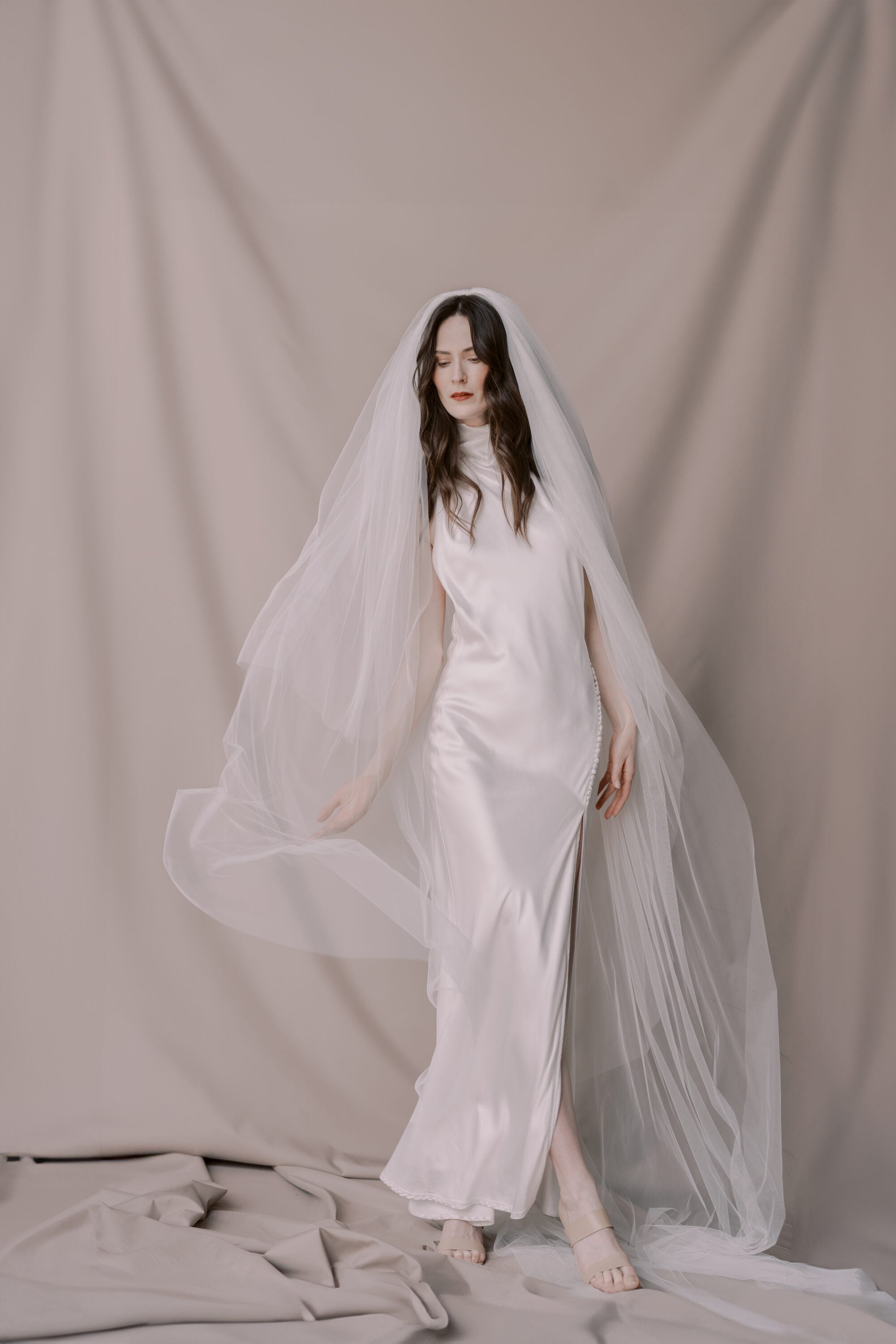 Woman wearing a white wedding dress with a long veil against a plain background