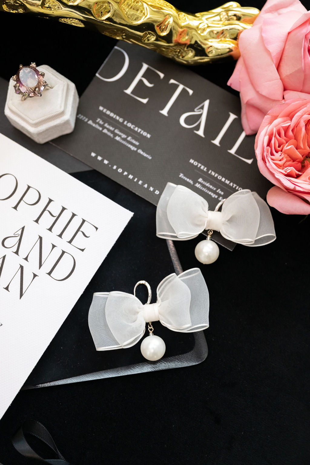 White bow earrings with pearls on a black card with floral and jewelry elements.