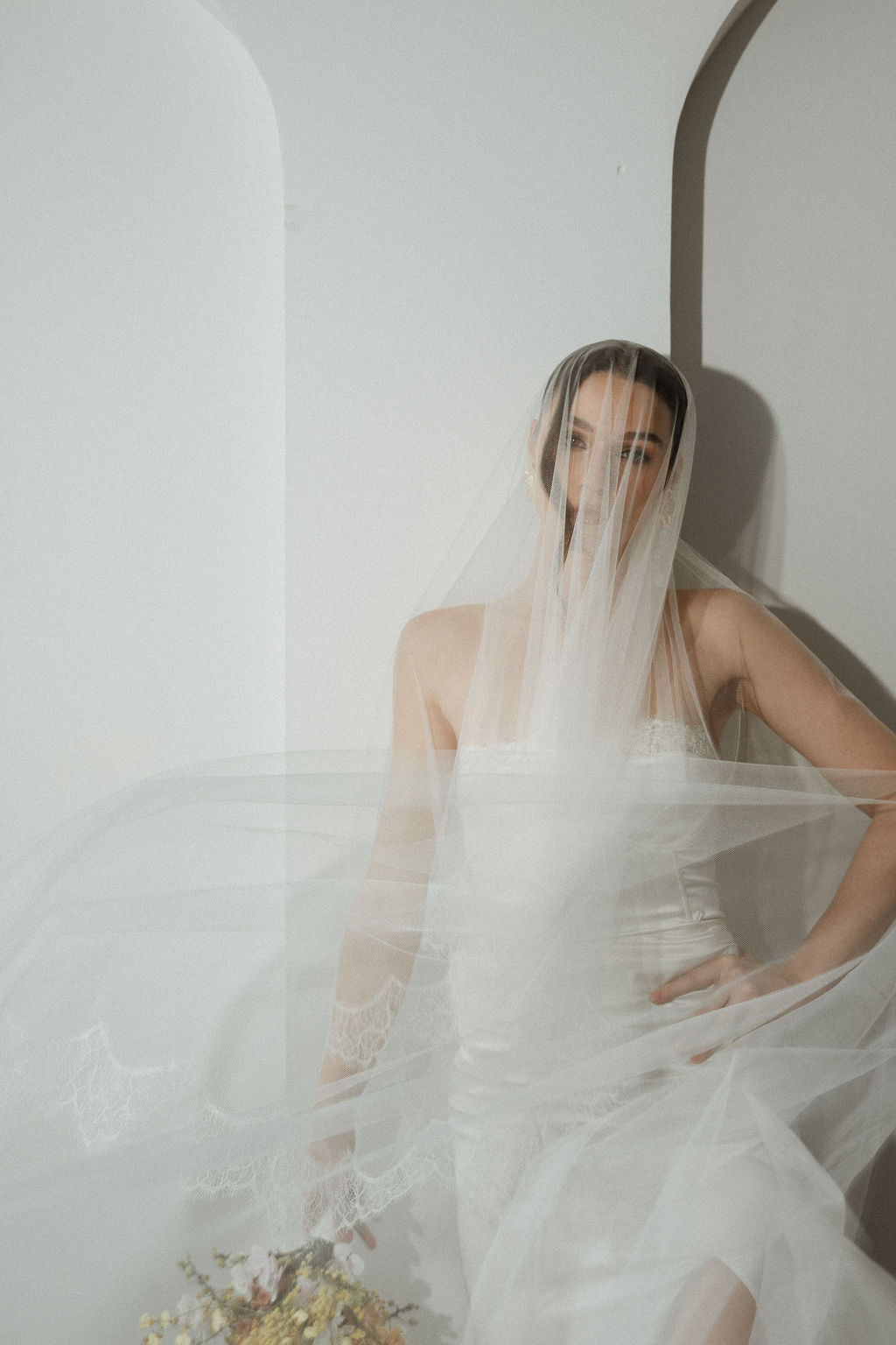 Woman in a wedding dress with a veil against a white wall