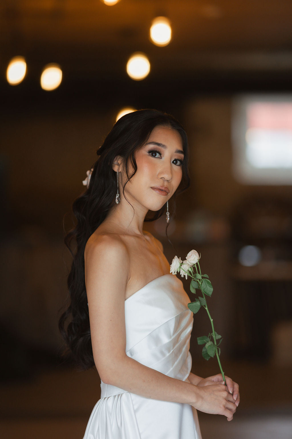 Woman in a white dress holding a single rose in a softly lit indoor setting