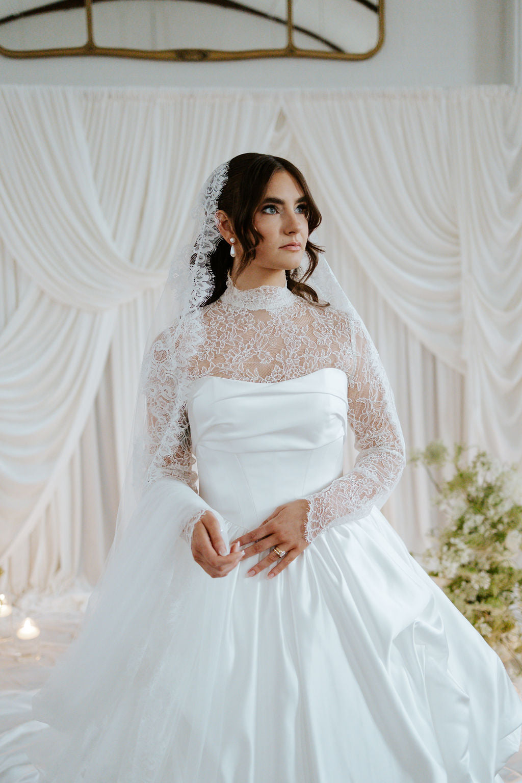 Woman in a white wedding dress with a lace veil against a decorative backdrop
