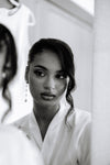 Black and white photo of a woman in a white robe looking at herself in the mirror.