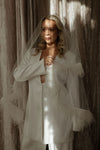 Woman in a white bridal outfit with a veil against a textured wall.