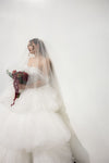Bride in a white wedding dress with a veil holding a bouquet against a plain background