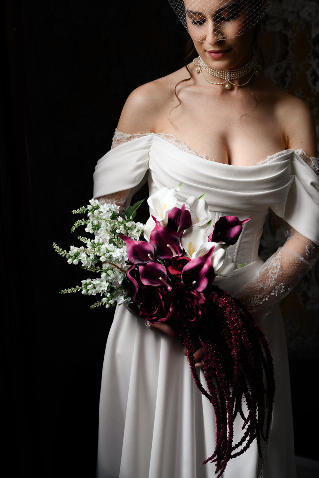Woman in a white wedding dress holding a bouquet against a dark background