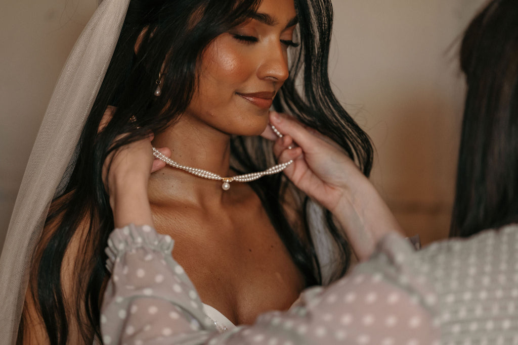 Woman adjusting a pearl necklace on another woman, with a blurred background