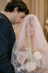 Man and woman embracing under a veil with floral decorations, possibly at a wedding.