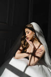 Bride in a white wedding dress with a veil, sitting against a dark background.