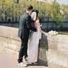 Couple in wedding attire standing on a bridge with a cityscape in the background