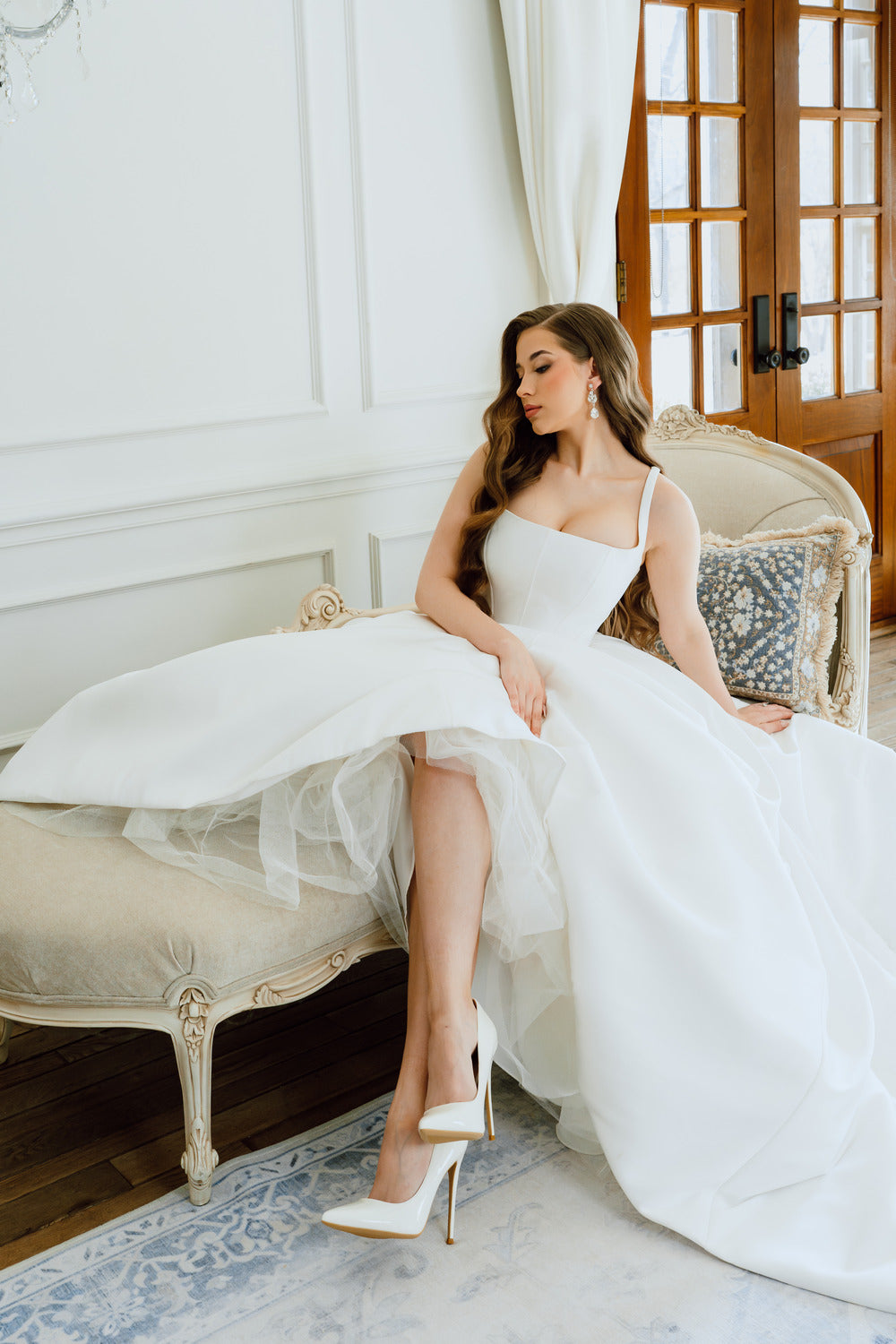 Woman in a white wedding dress sitting on a vintage chair in a elegant room.