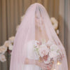 Bride holding a bouquet under a soft pink veil with floral decorations in the background