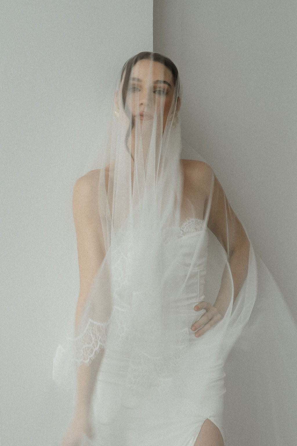 Woman in a white wedding dress with a veil against a plain background