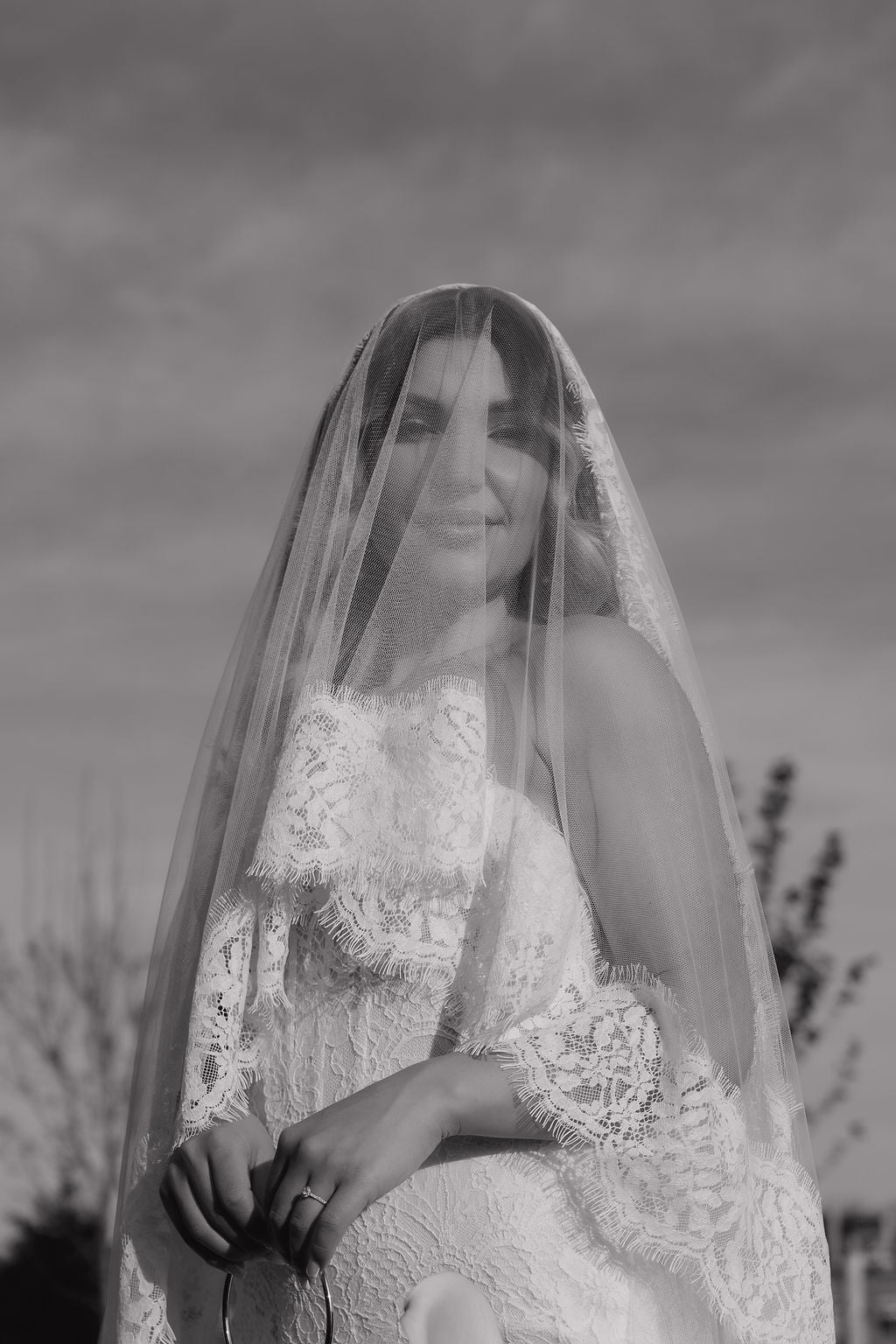 Black and white photo of a bride with a long veil against a natural background