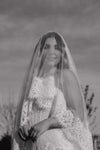 Black and white photo of a bride with a long veil against a natural background