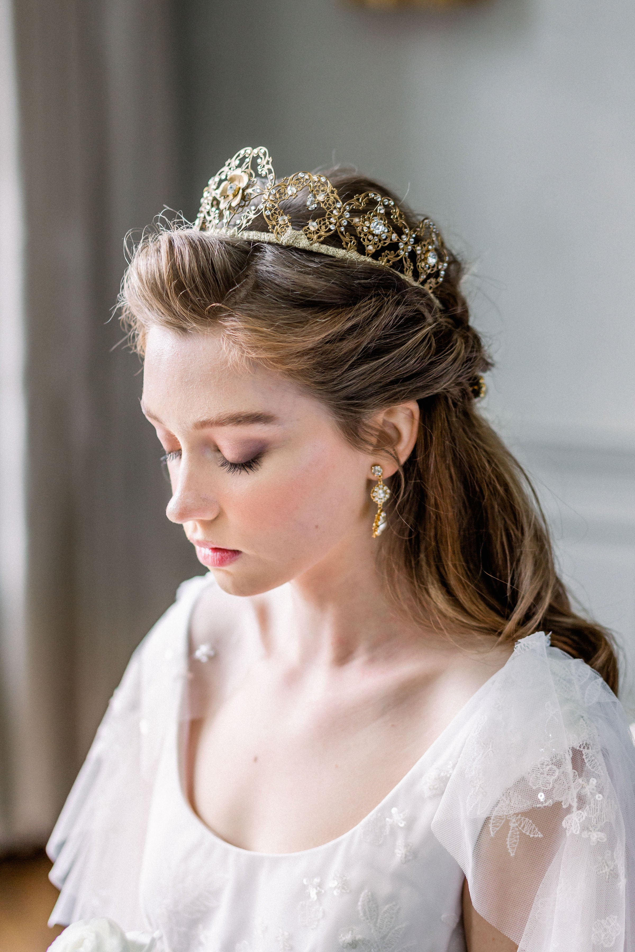 Woman wearing a gold tiara and earrings in a softly blurred indoor setting