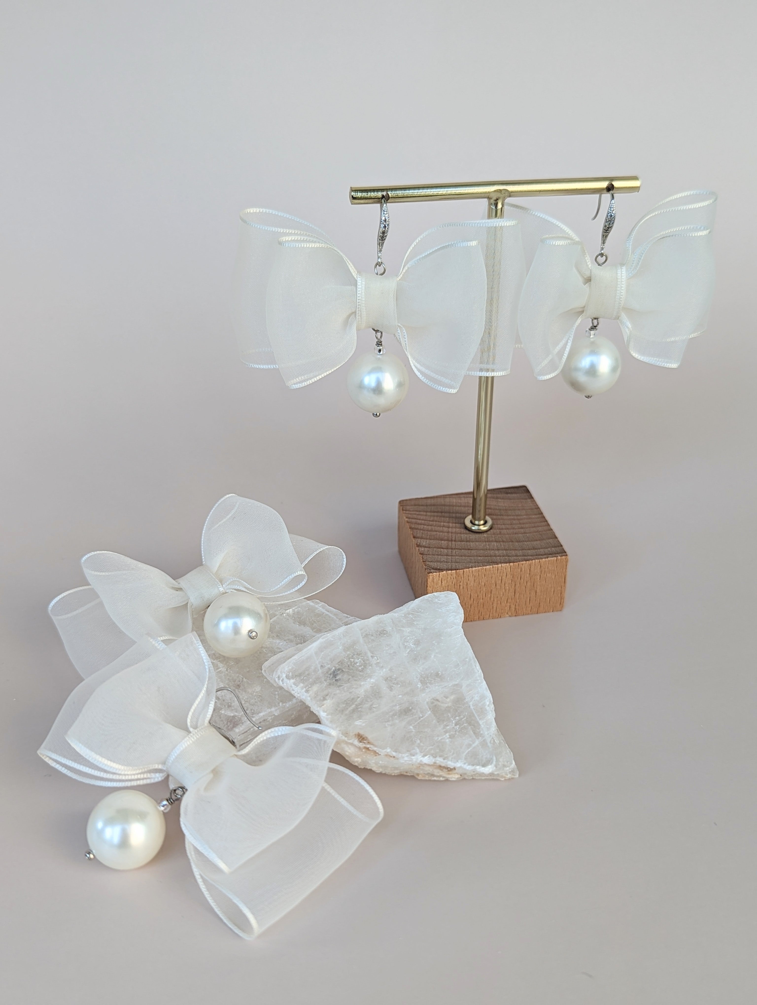 organza ribbon bow earrings with pearl accents on a stand against a light background