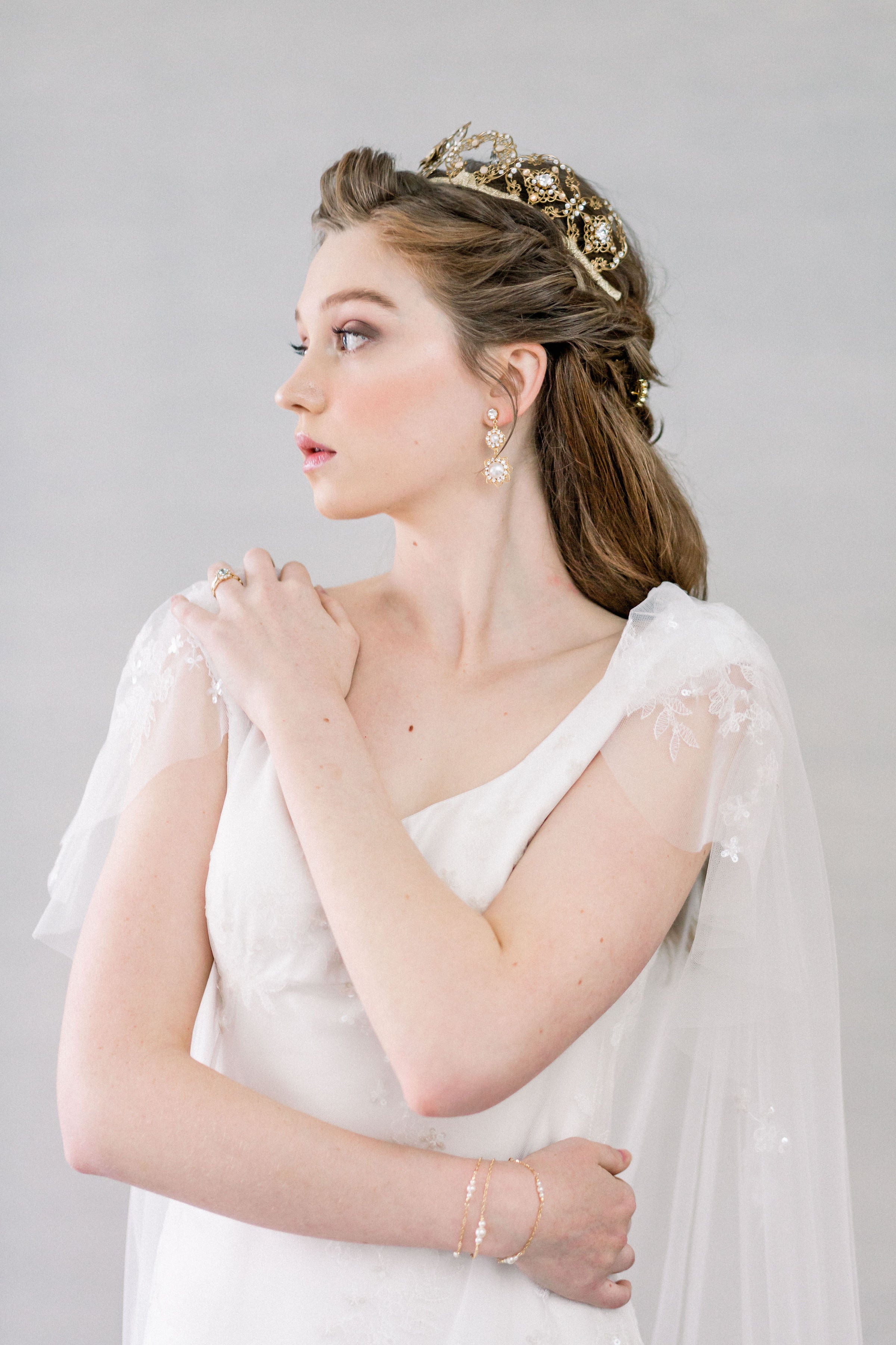 Woman in a white wedding dress with a gold tiara and veil against a gray background