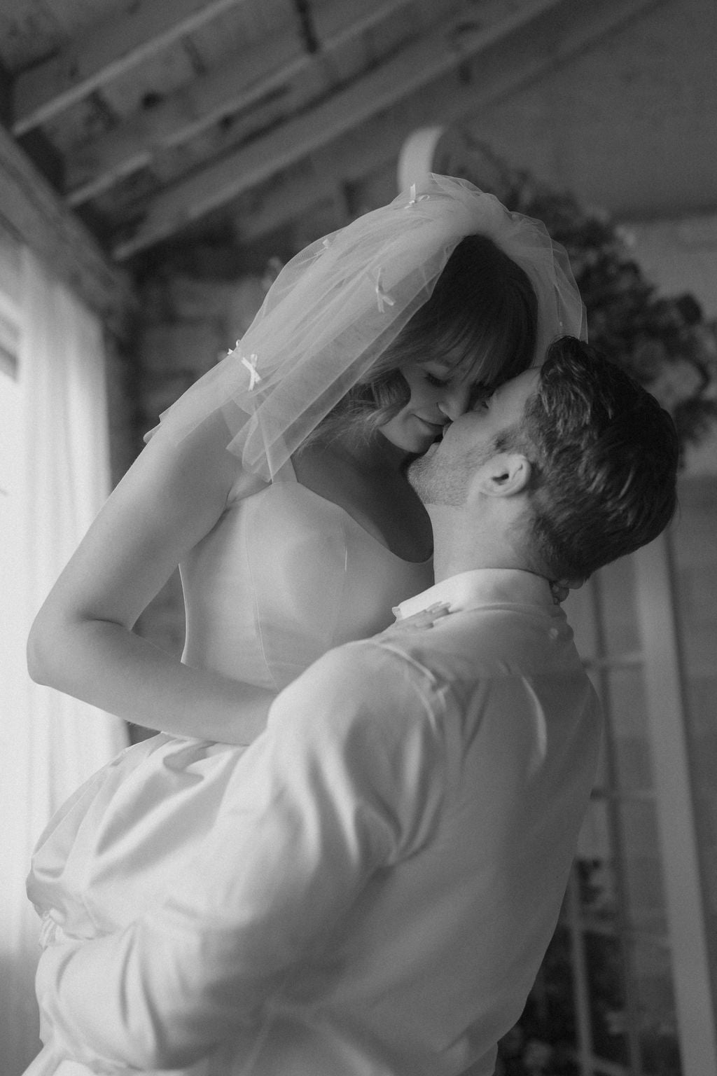 Black and white photo of a couple embracing under a veil.