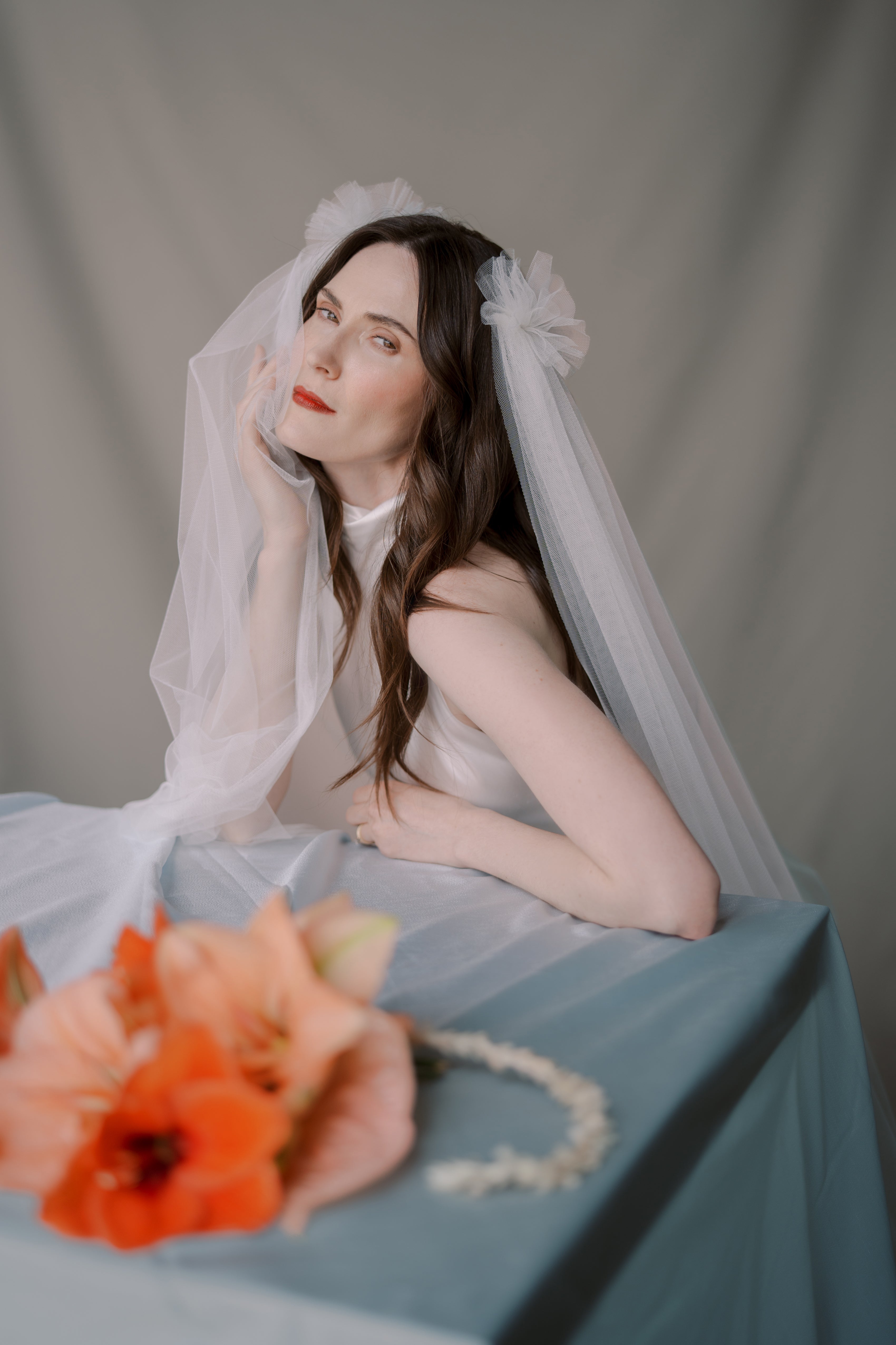 Woman in a bridal outfit with a veil and bouquet on a gray background