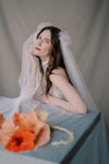 Woman in a bridal outfit with a veil and bouquet on a gray background