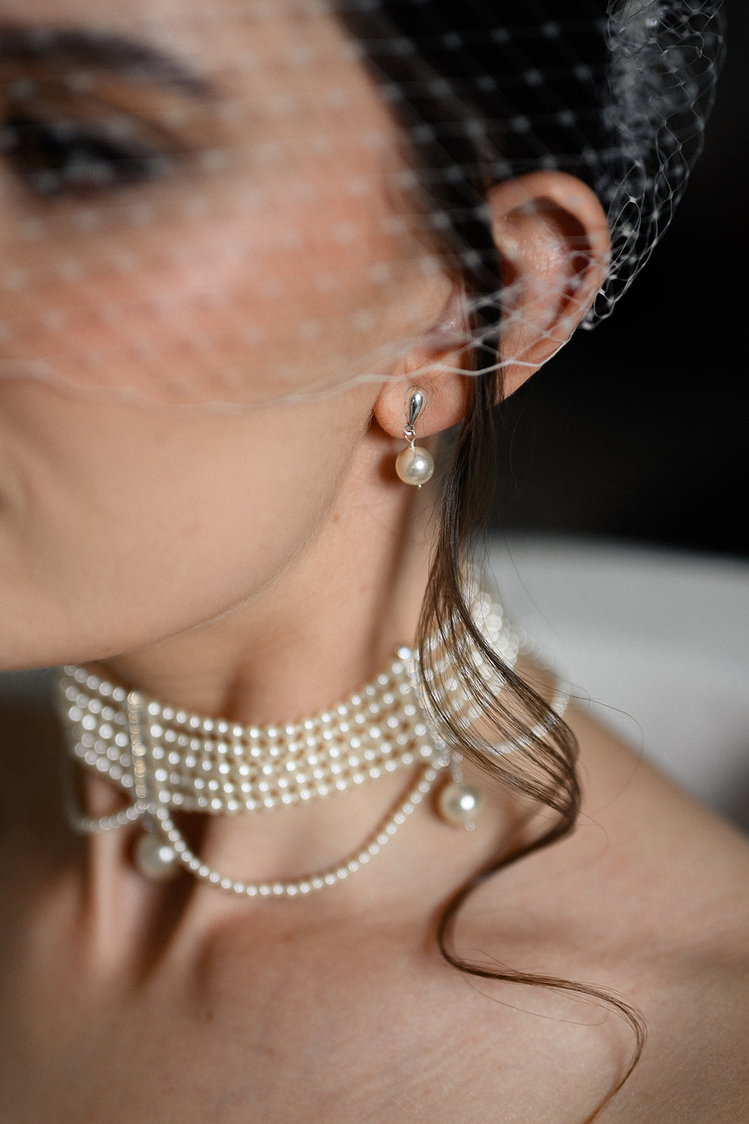 Close-up of a woman wearing pearl earrings and a necklace with a dark background