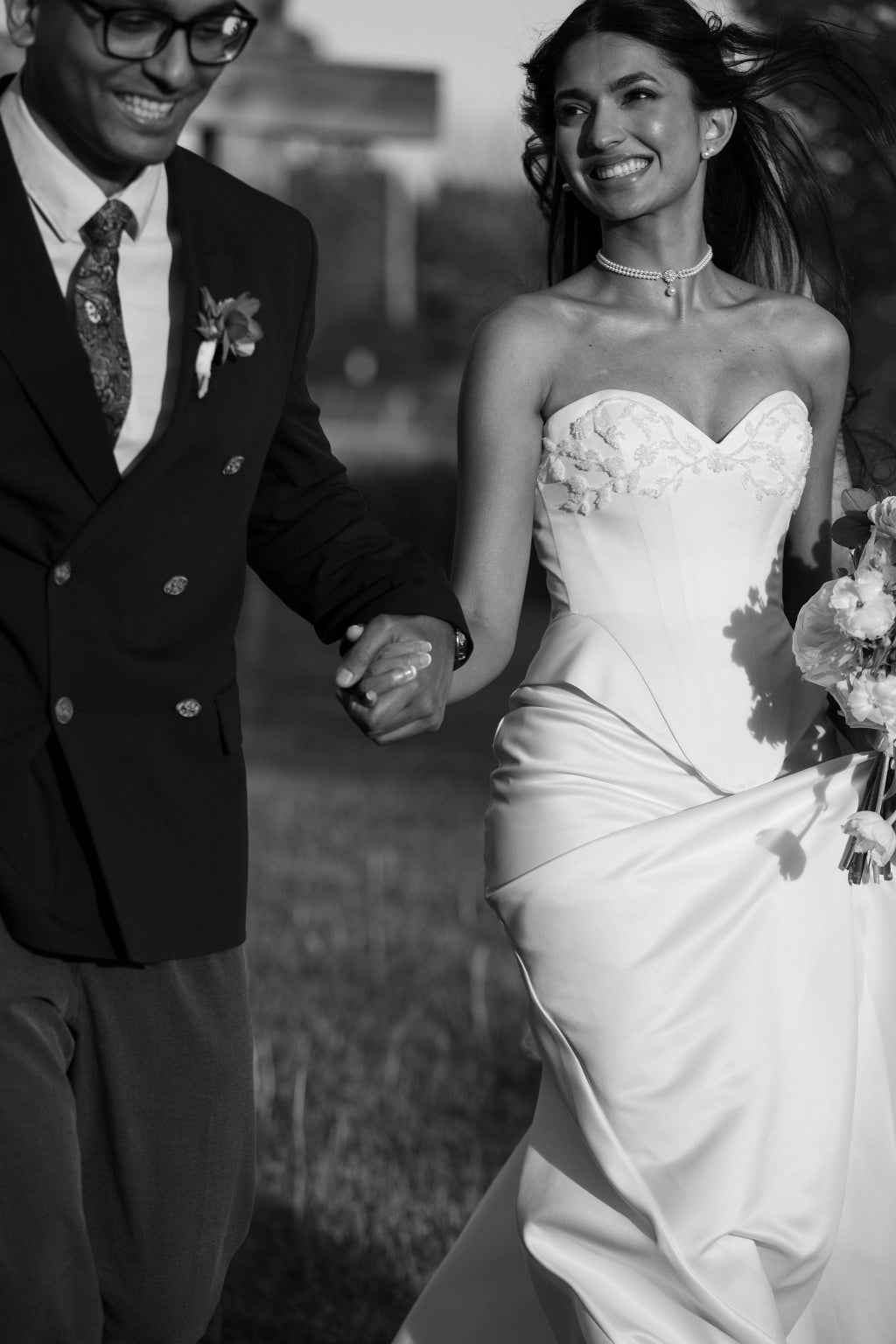 Black and white photo of a couple holding hands, likely at a wedding.