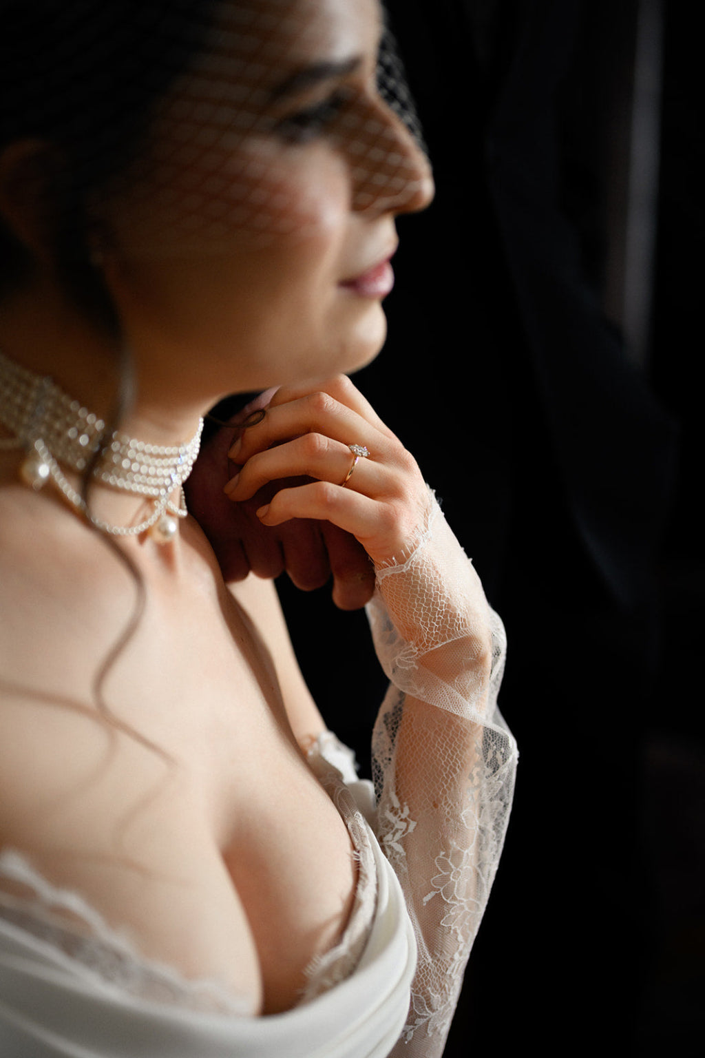 Woman in a wedding dress with lace sleeves and veil, looking away from the camera.
