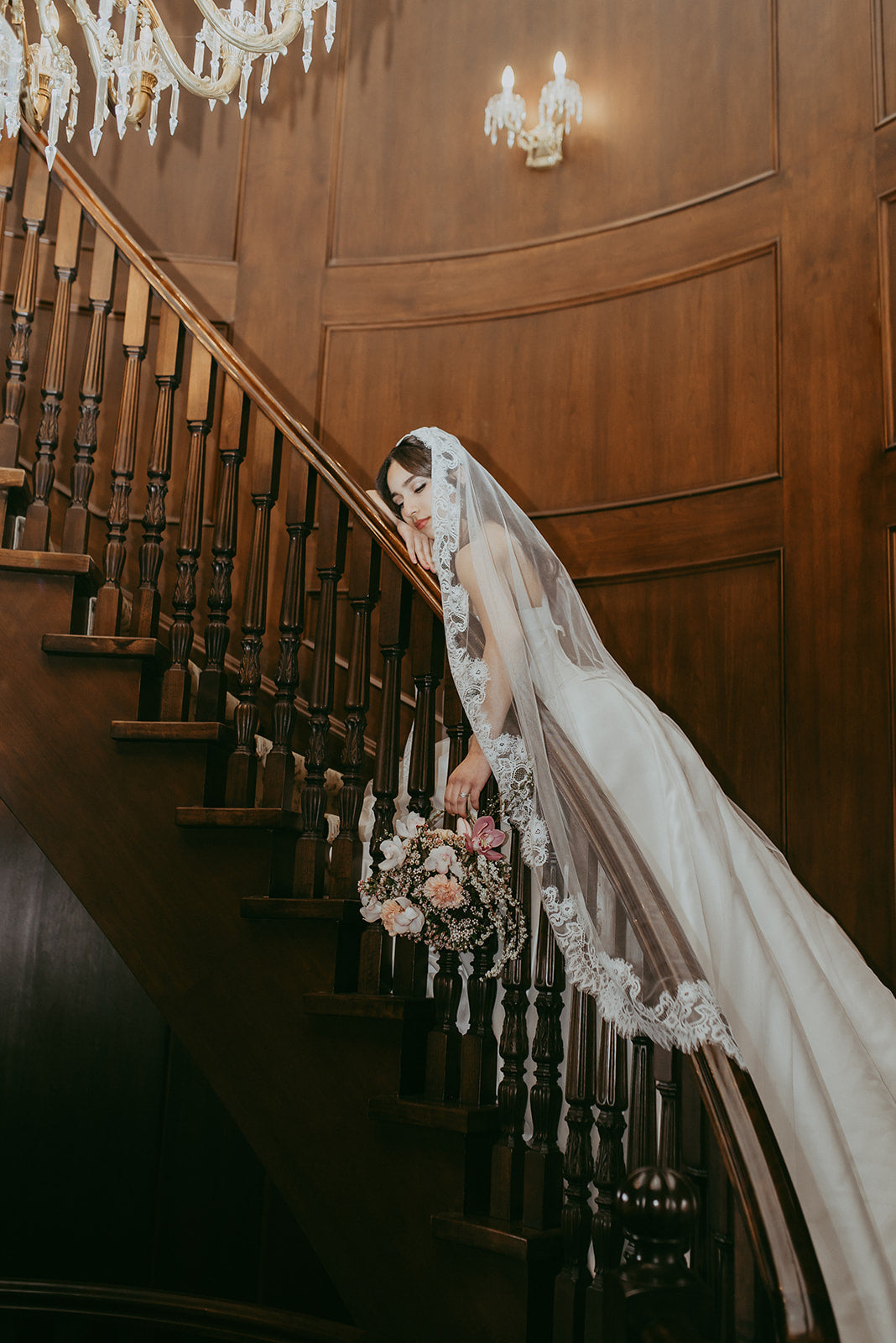 Bride with a bouquet standing on a staircase in an elegant indoor setting