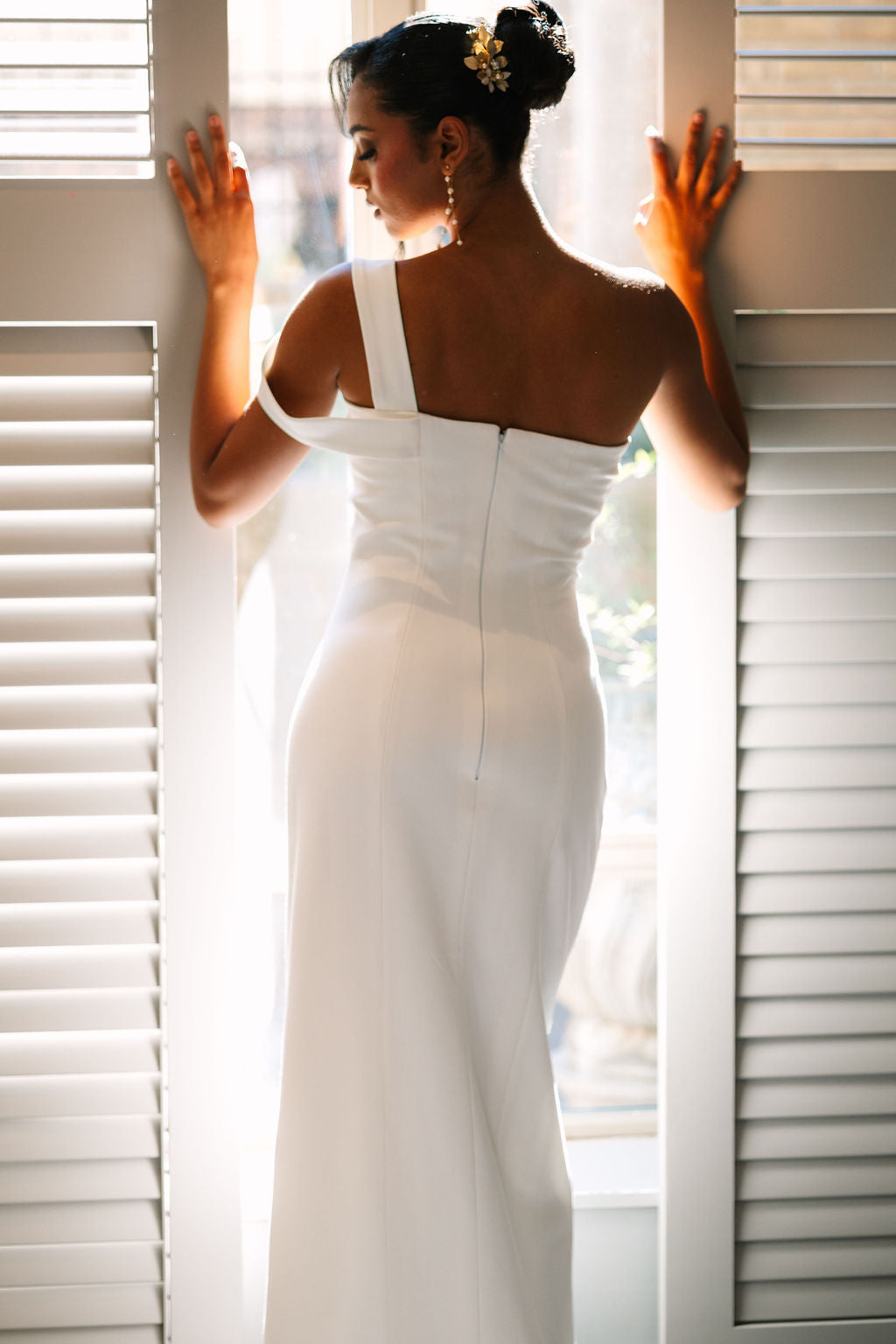 Woman in a white wedding dress standing between two white shutters.